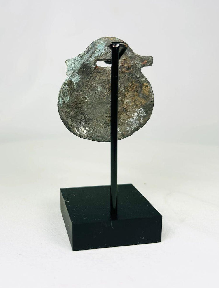 Photograph of back view of rounded Roman bronze pendant used as a protective or symbolic charm.