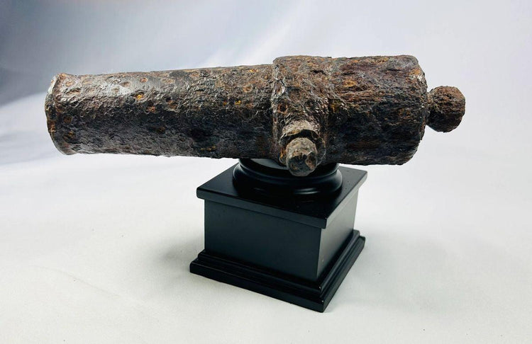 Side view of an excavated 18th-century British signal cannon displayed on a black museum stand.