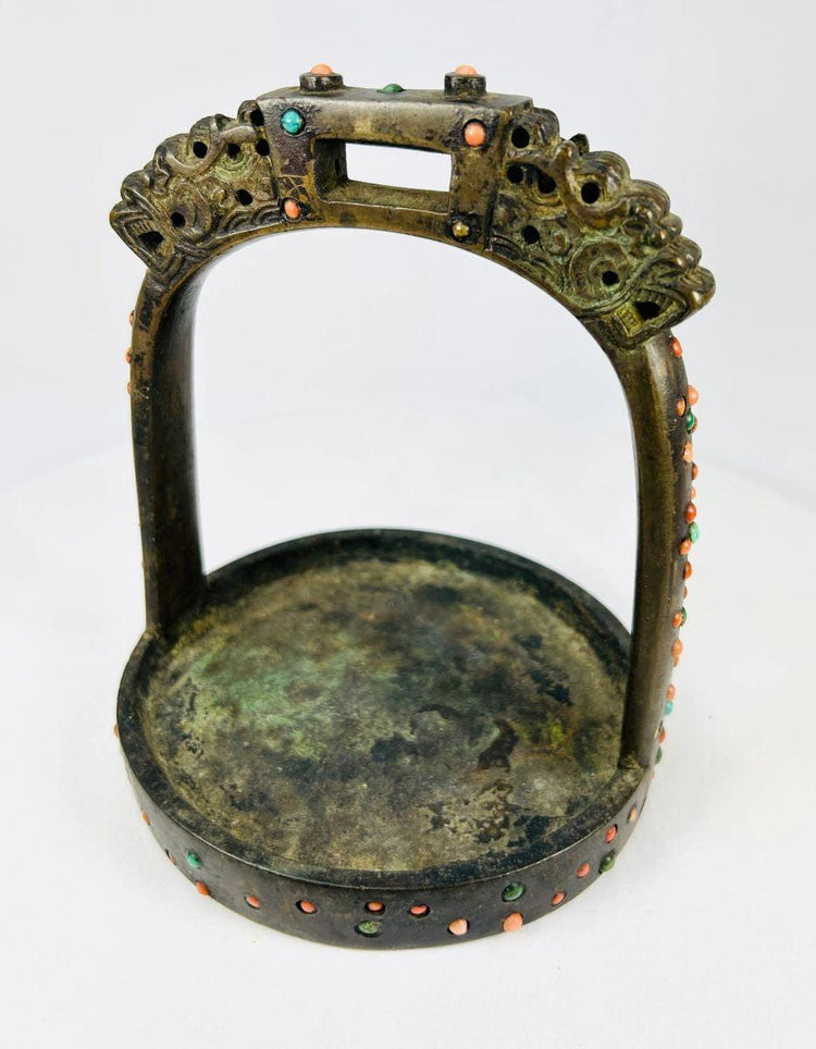 Close-up of dragon-motif bronze stirrup showing stone inlay and aged patina.