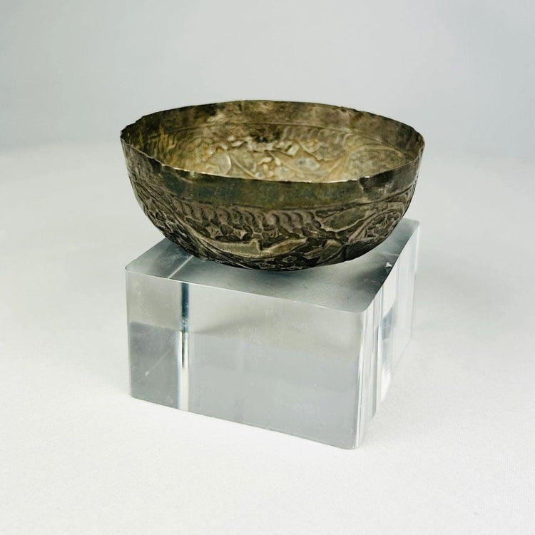 Seljuk Persian silver unguent bowl from the 12th–13th century CE, side profile view showing intricate engraved floral and geometric designs with aged silver patina, positioned on a clear display base under neutral studio lighting