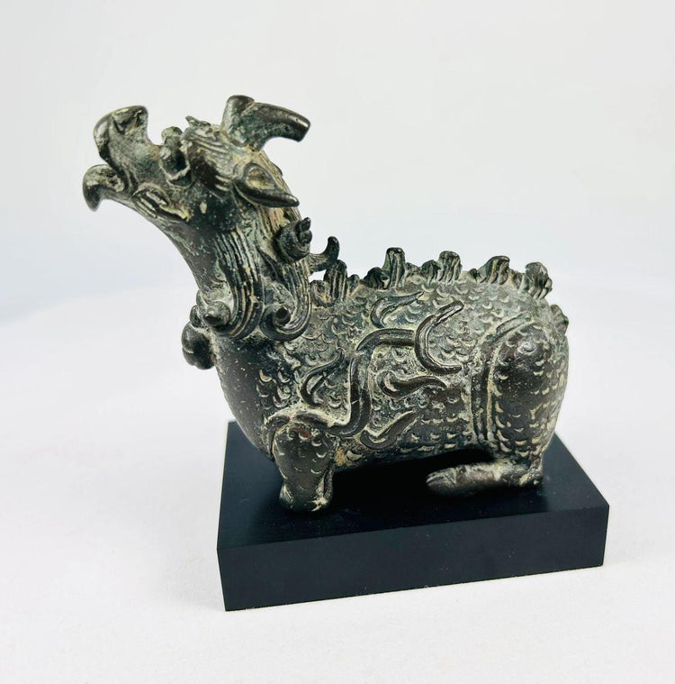 Bronze Qing Dynasty Qilin censer on black museum stand, showing detailed flame-scroll body and open mouth for incense release.