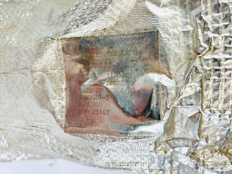 Close-up of identification label on flown NASA Space Shuttle blanket insulation panel, showing stamped details including April 1983 date, serial number S/N 008, and manufacturer code MFR 25167, used in the shuttle’s Thermal Protection System.