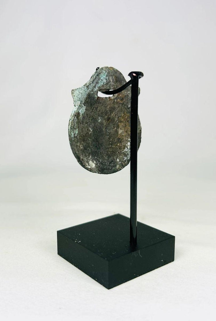 Angle view of ancient Roman bronze amulet showing oxidized surface and fine engravings.