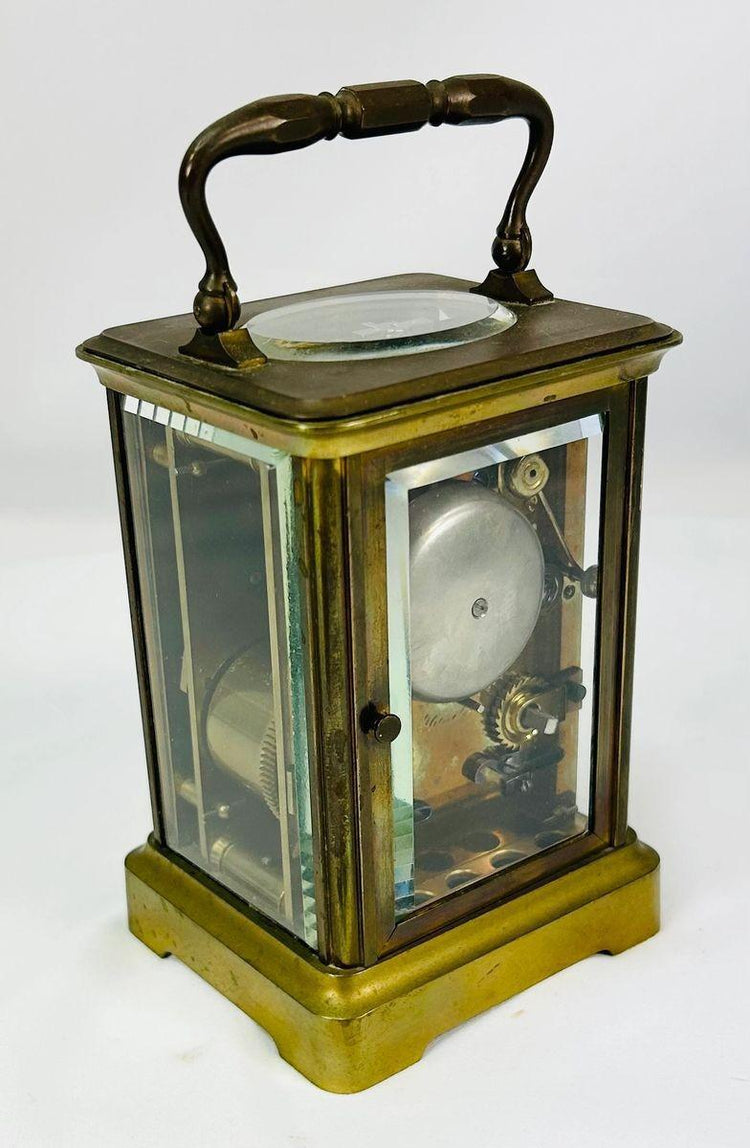 Side angle of 19th-century brass carriage clock highlighting beveled glass and patina.