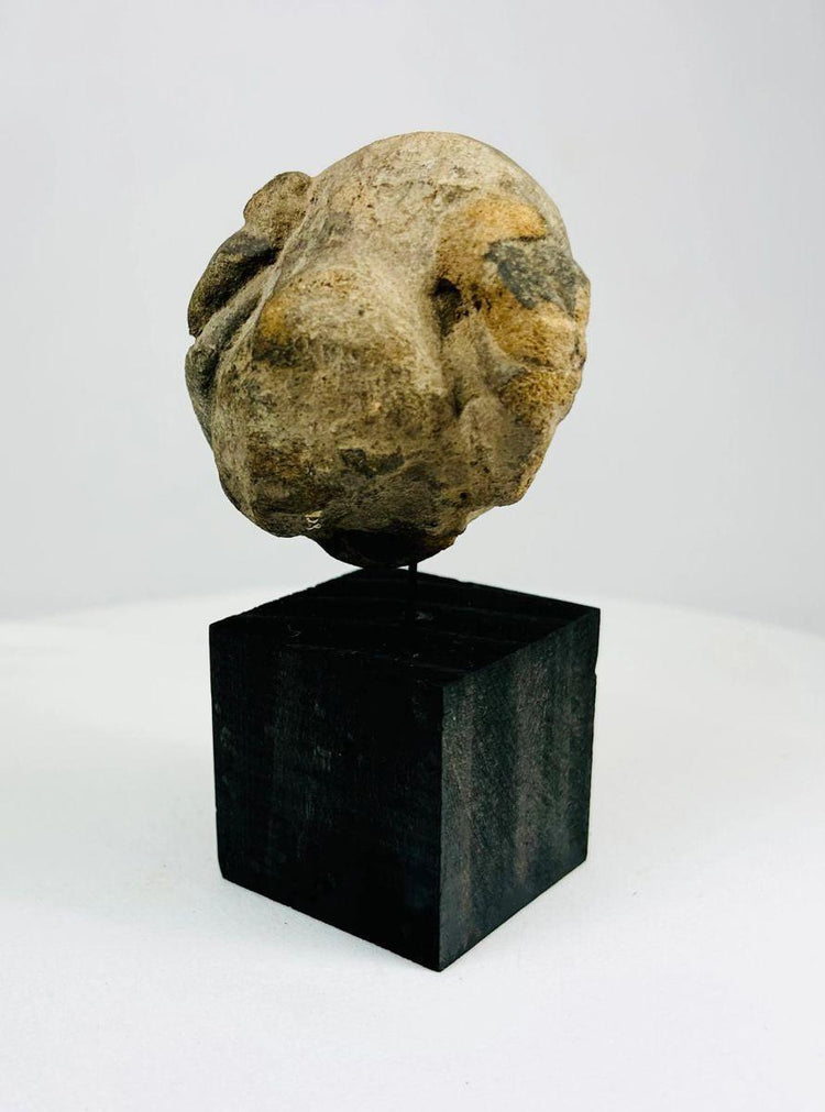 Ancient carved stone mask fragment mounted on black wooden stand