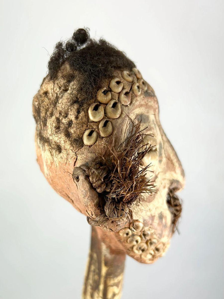 Sepik River ceremonial dagger with carved ancestral head, cowrie shell inlays, and human hair, left-angled view showcasing facial details and tribal motifs.