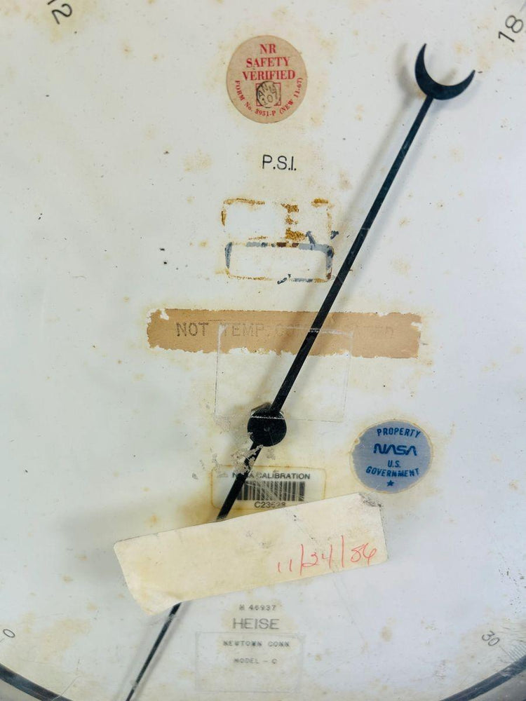 Close-up of NASA Space Shuttle low-pressure gauge face, showing calibration seals, Heise manufacturer mark, and original service sticker dated 11/24/86, used for shuttle ground support operations in the 1980s.