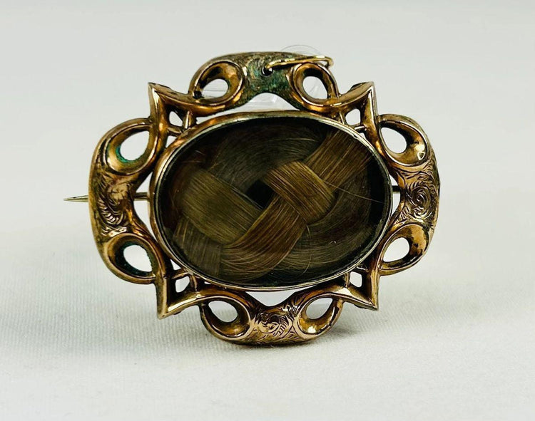 Museum-style photograph of a mid-19th-century Victorian mourning hairwork brooch.