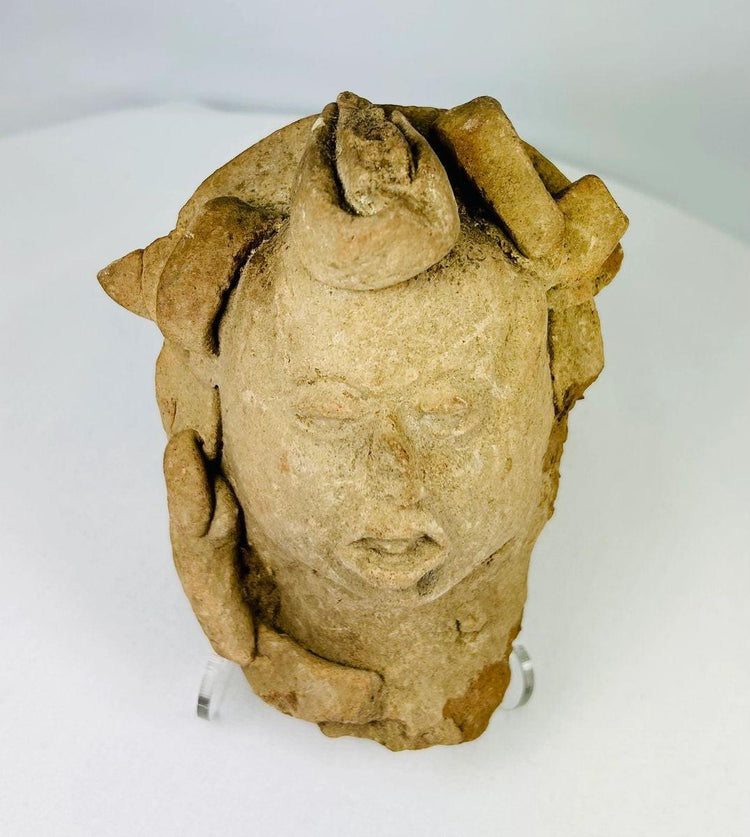 Mesoamerican terracotta head artifact displayed on stand, archaeological-style photograph