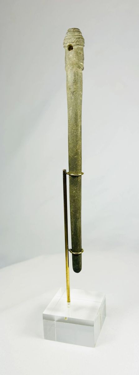 Angled view of an ancient Bactrian stone idol with Janus-style human head and elongated form, mounted upright on a modern display stand.