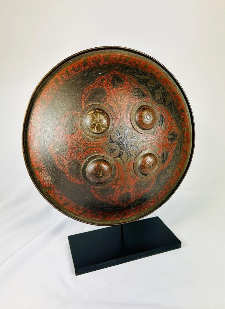 Indo-Persian lacquered dhal shield with four brass bosses and red foliate motifs displayed on stand.8297
