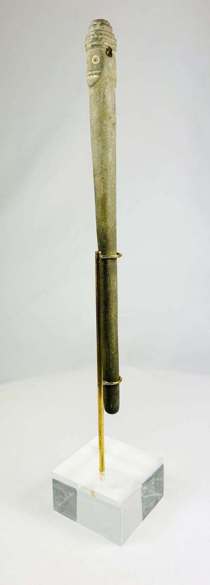 Side view of an ancient Bactrian stone idol with Janus-style human head and elongated form, displayed upright on a modern stand.