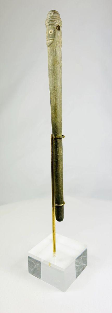 Side view of an ancient Bactrian stone idol with Janus-style human head and elongated form, displayed upright on a modern stand.