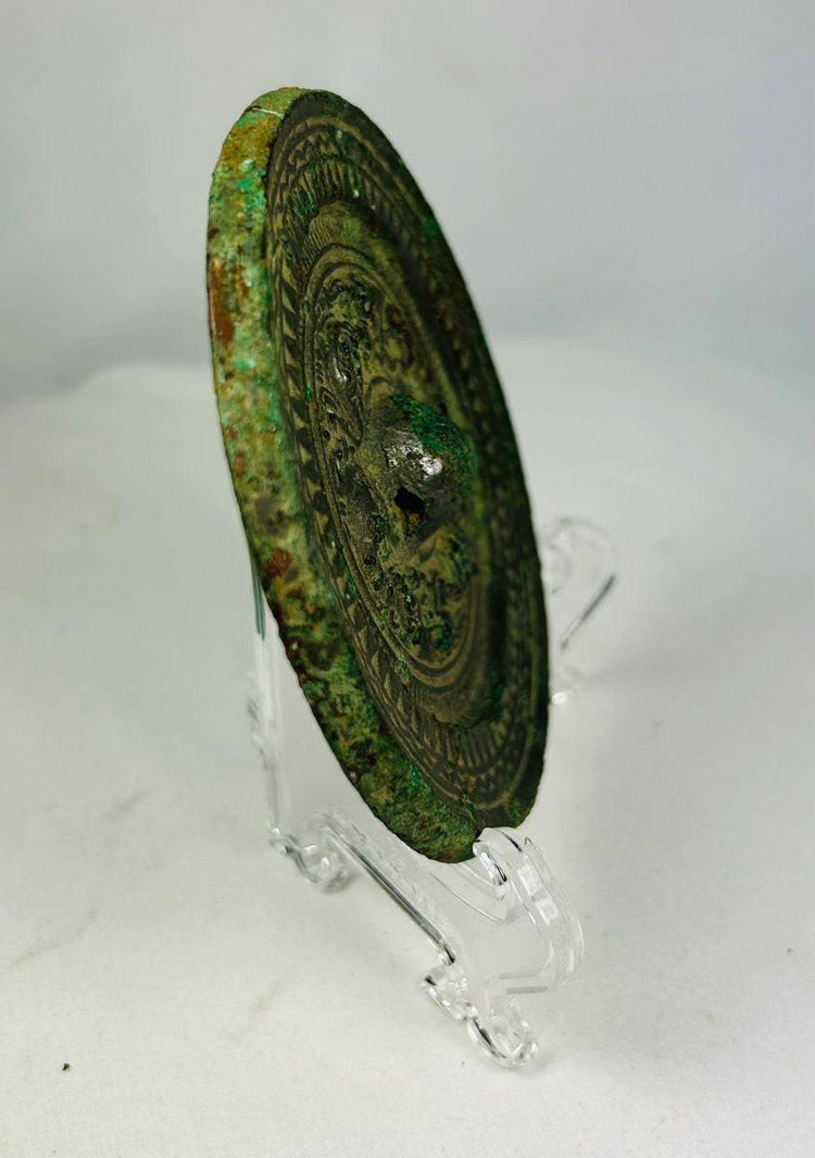 Side view of ancient Chinese bronze mirror displaying concentric decorative bands and preserved patina.