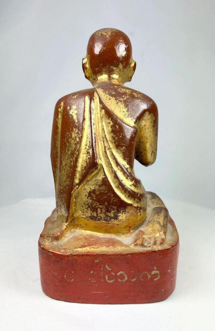 Close-up of red lacquer pedestal supporting the Burmese monk statue, showing aged texture and hand-carved form.