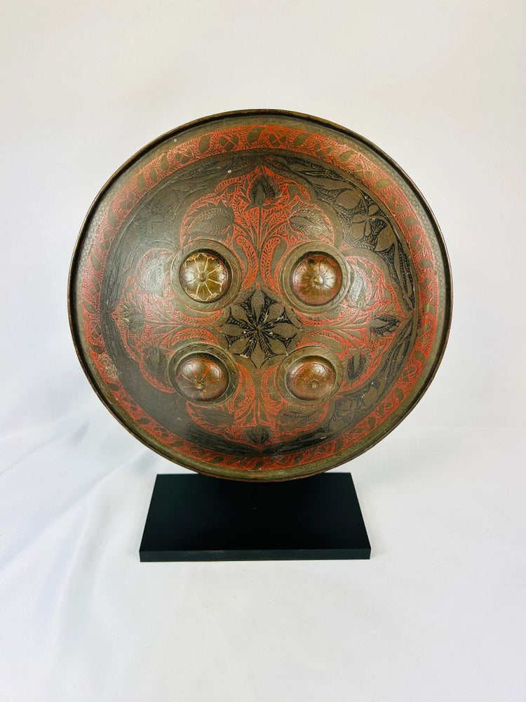 Antique Indo-Persian dhal shield showing damascened patterns and four domed bosses on display stand.