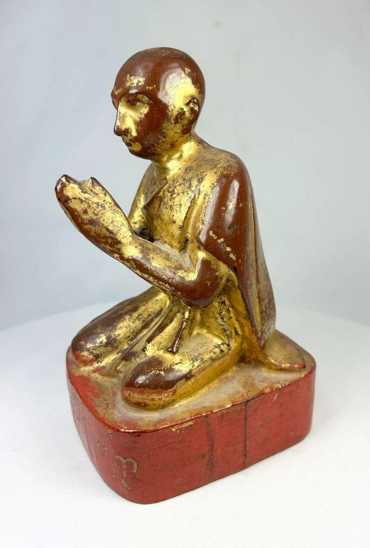 Side profile of antique Burmese Buddhist monk sculpture showing carved robe details and gilded surface.