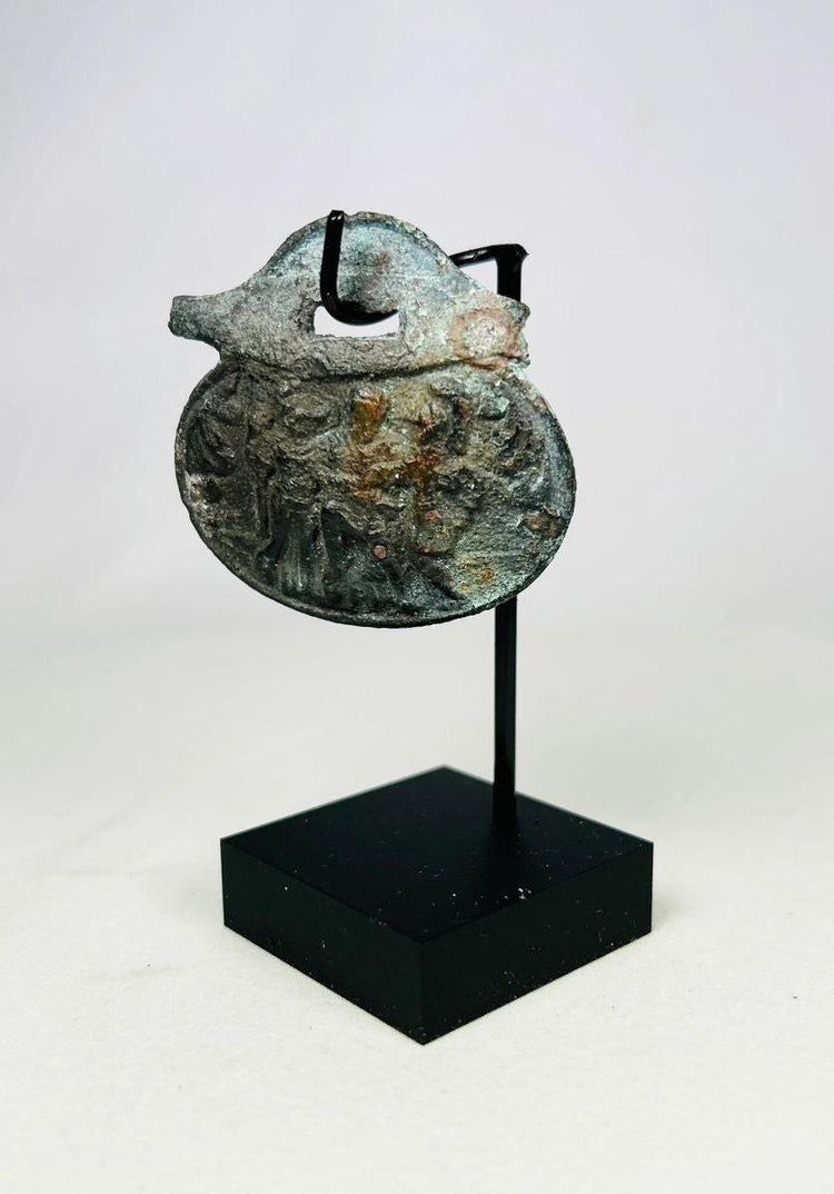 Close-up of Roman bronze pendant showing three standing figures, one helmeted.