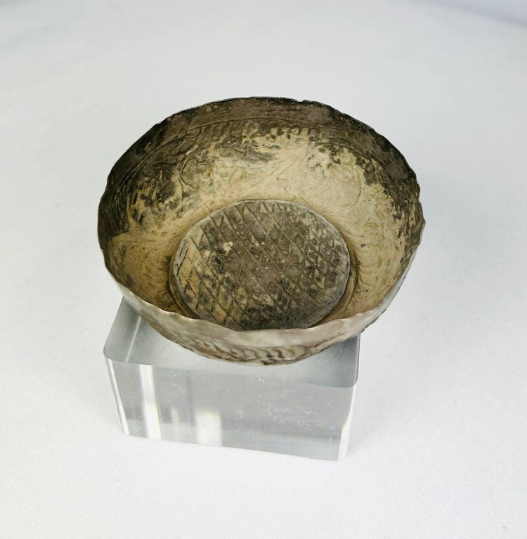 Overhead view of Seljuk Persian silver unguent bowl from the 12th–13th century CE, revealing the detailed engraved interior with geometric lattice design and aged patina, displayed on a transparent acrylic stand.