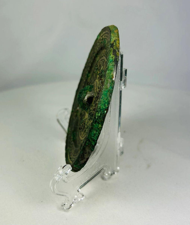 Bronze mirror from the Han Dynasty with intact central boss and verdigris patina.