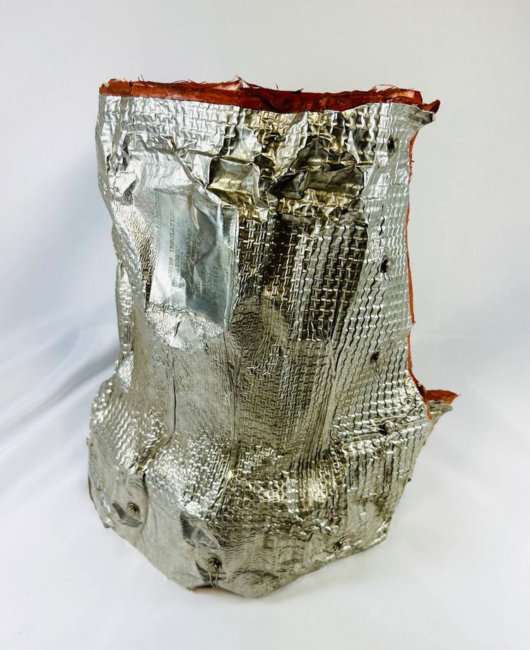 Authentic flown NASA Space Shuttle blanket insulation, made of fibrous silica batting with reflective metallic surface and orange edge trim. Stamped April 1983 with manufacturer code and serial number, used in the orbiter’s Thermal Protection System for pitch actuator thermal shielding.