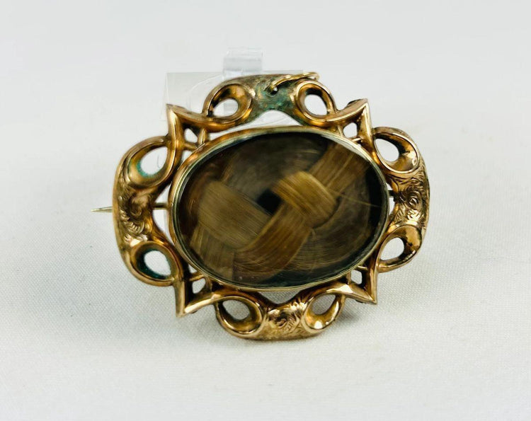 Victorian mourning hairwork brooch with braided human hair beneath beveled glass, mid-19th century.