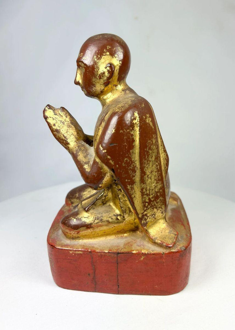Full-height image of antique gilded Buddhist monk figure displayed on red lacquer pedestal.