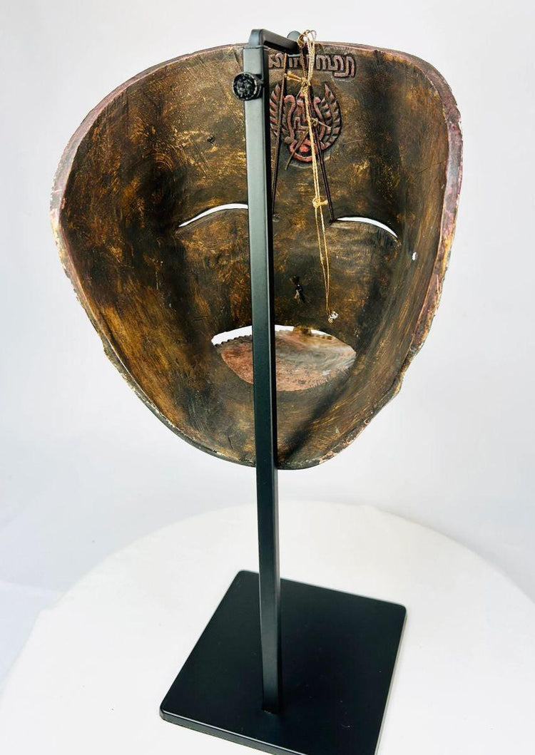 Back view of a late 19th-century Javanese carved wooden Cakil mask showing interior surface and hanging cord on a black display stand.