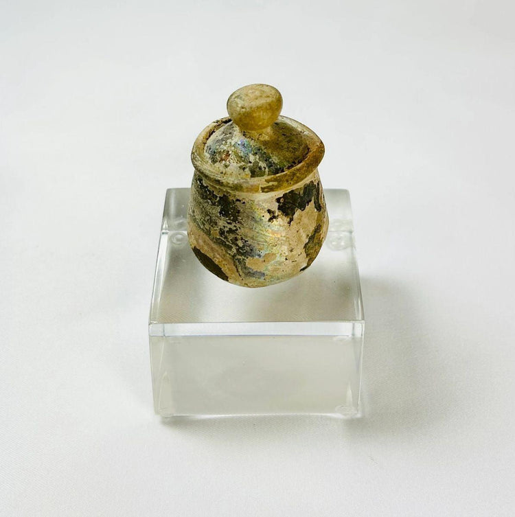 Ancient Middle Eastern glass cosmetic jar with iridescent surface and intact lid, 2nd–3rd century AD.