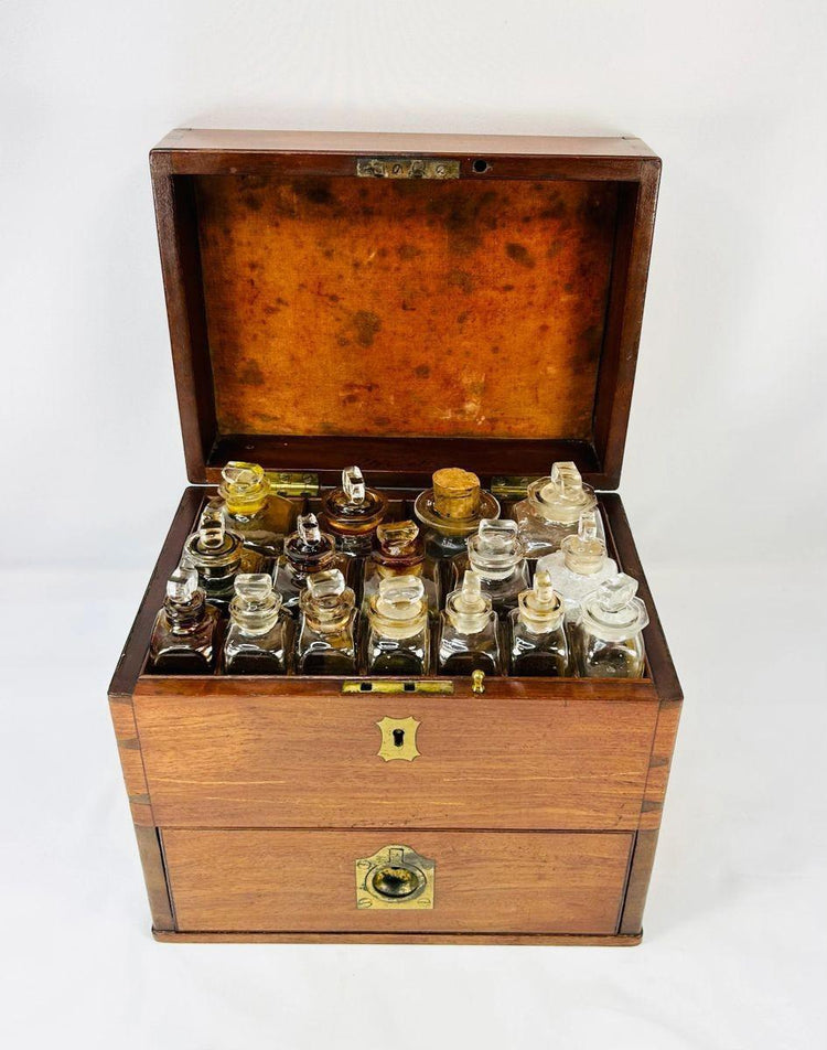 Antique Victorian apothecary box with drawers open, displaying glass bottles, brass scales, mortar and pestle, and chemist’s tools — 19th-century England.