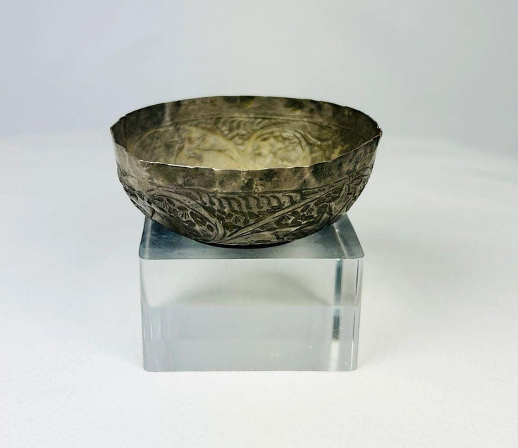 Seljuk Persian silver unguent bowl from 12th–13th century CE, featuring intricate engraved floral and geometric motifs with a natural silver patina, displayed on a clear acrylic stand under studio lighting.