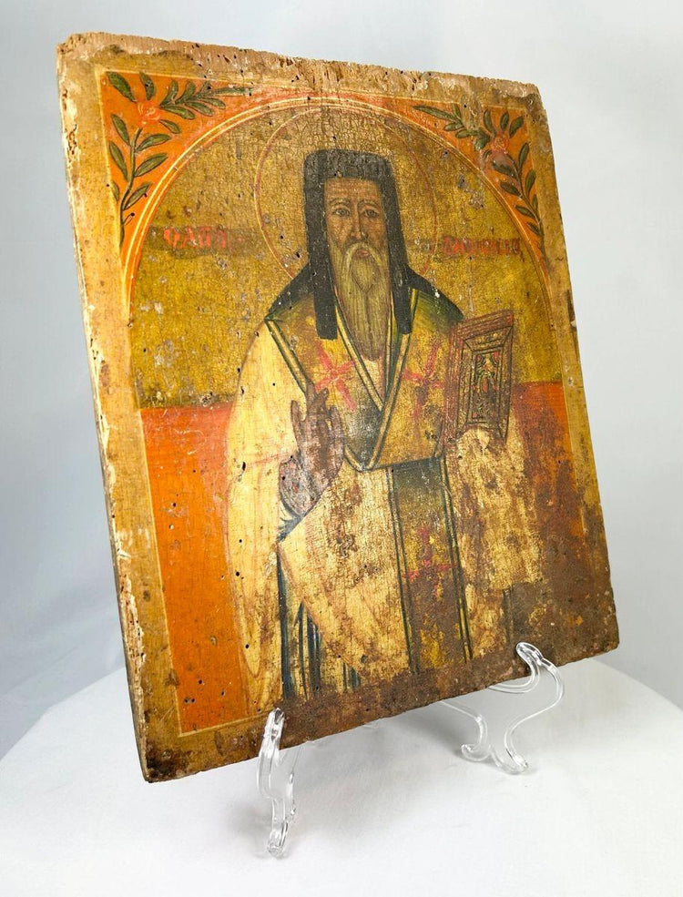 Angled view of an 18th-century Russian Orthodox icon showing a saint holding a Gospel book, hand-painted on an aged wooden panel.