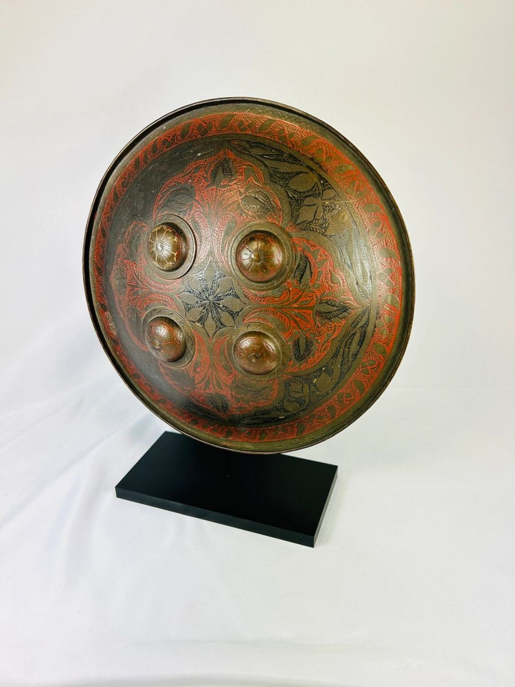 19th-century Indo-Persian warrior shield featuring intricate red and black lacquer designs and raised bosses.