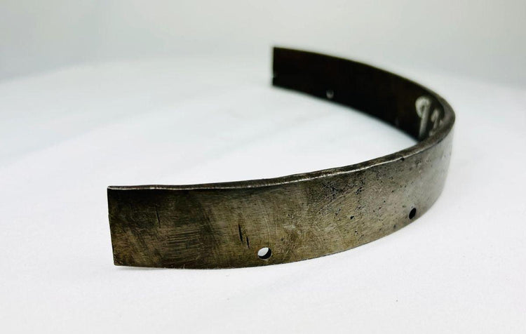Front view of 17th-century European forged steel armor segment showing curved defensive band and aged metal surface.