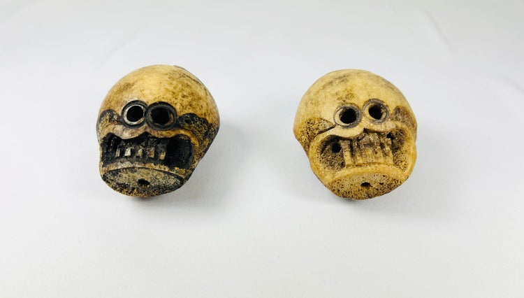 Pair of Tibetan Kapala Citipati skull beads with carved teeth and eye sockets, photographed from a forward angle on white cloth.