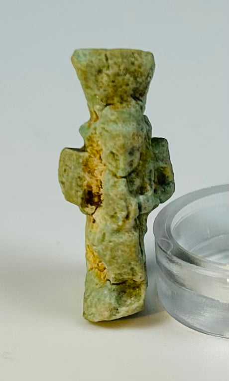 Ancient Egyptian protective Bes charm in glazed faience mounted on display stand.