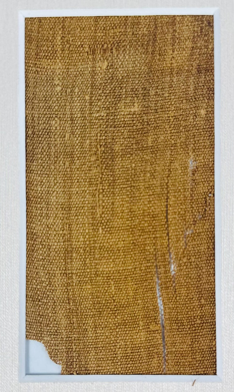 Close-up of the larger attributed mummy-wrapping fragment, showing woven linen texture, frayed edges and narrow separations.