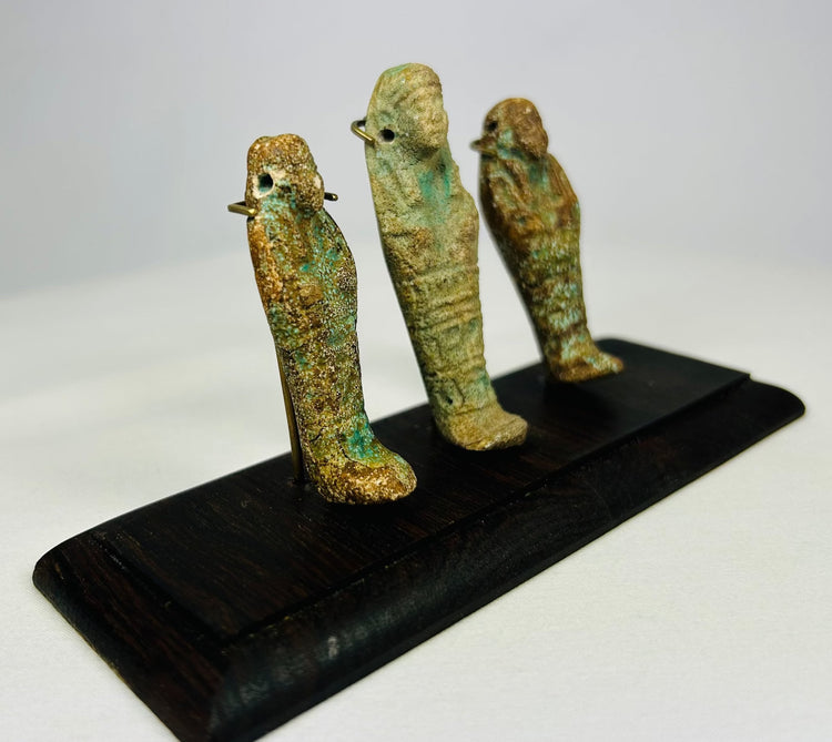 Three ancient Egyptian faience ushabti figures viewed from a diagonal angle on a black wooden display base.