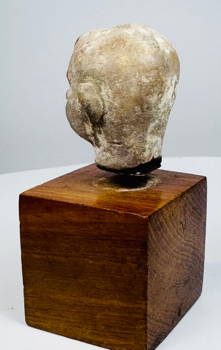 Ancient terracotta head with a rounded crown, weathered surface, and uneven neck edge above a brown wooden display base.