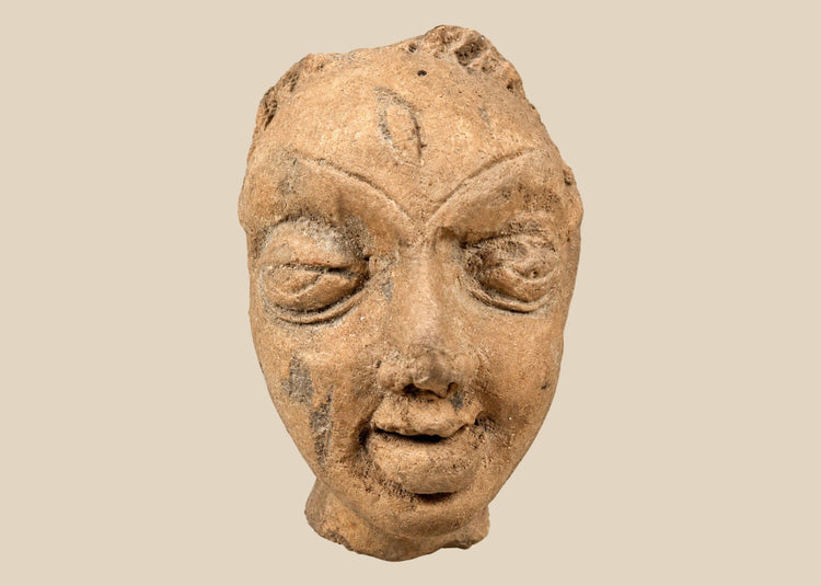 Gupta-period Northern Indian terracotta head fragment with serene almond-shaped eyes, arched brows, and softly smiling lips, warm earthen tones with mineral deposits, 3rd–5th century CE, mounted on modern display stand for preservation.