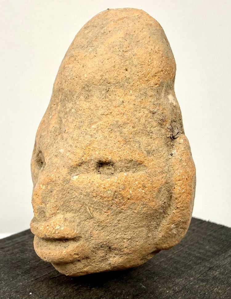 Frontal close-up of stylized terracotta face with almond-shaped eyes and weathered orange-brown ceramic
