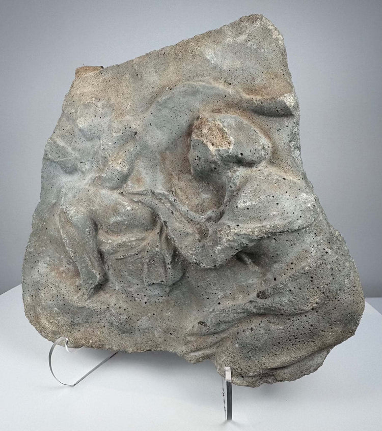 Roman relief fragment in gray volcanic tuff showing weathered human figures and naturally pitted stone surface