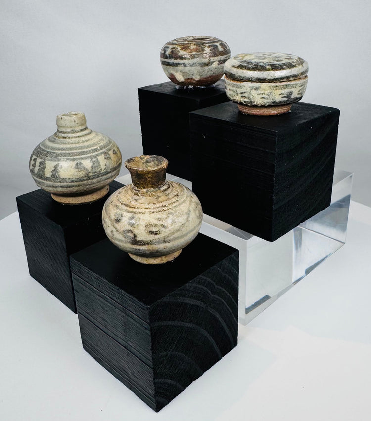 Four miniature Thai stoneware containers with transparent glaze and painted ornamentation, mounted on custom display stands.