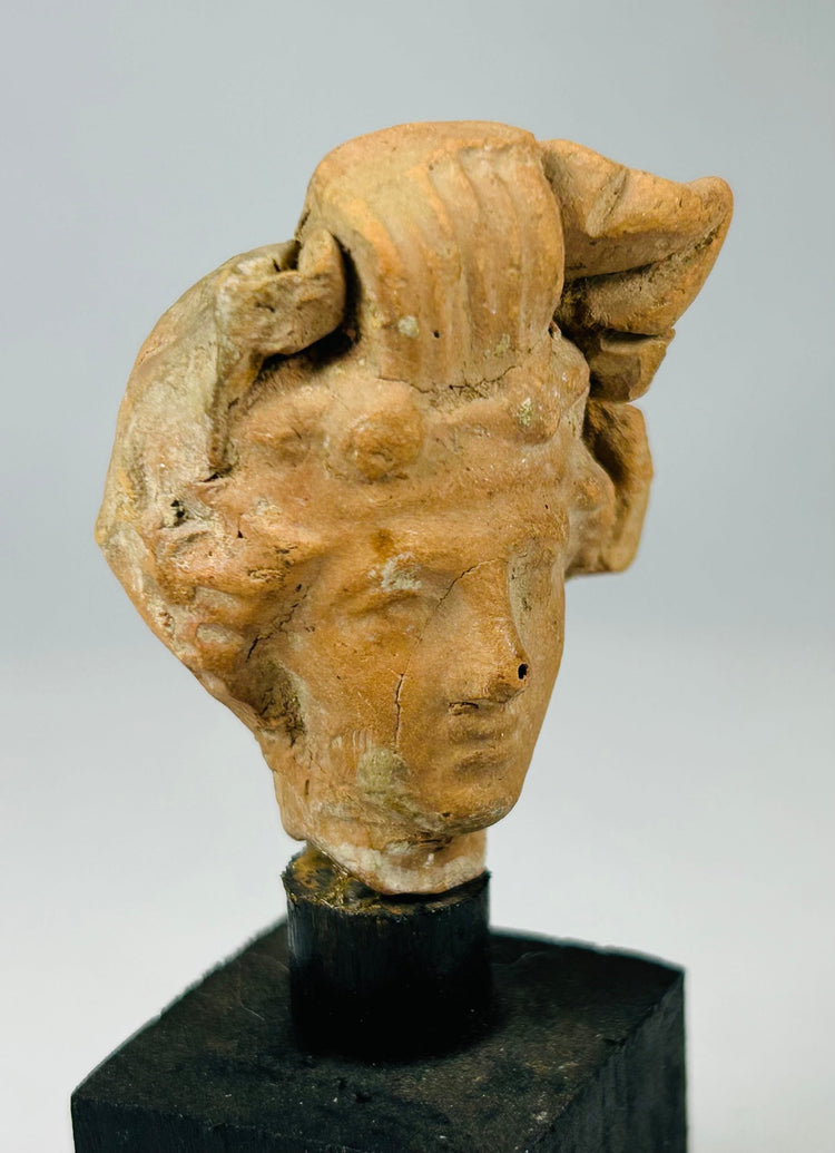 Ancient Roman or Hellenistic terracotta figurine head with worn surface, preserved features, and historical character.