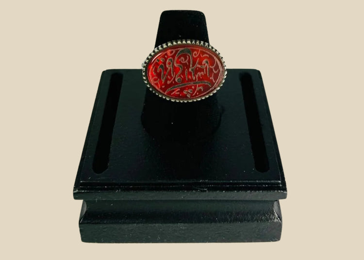 Oval carnelian intaglio ring from the Ancient Near East, 1st millennium BCE. Features engraved animal and symbolic motifs on red carnelian, set in a silver bezel, displayed on a black stand. Excellent condition with finely detailed intaglio carvings.