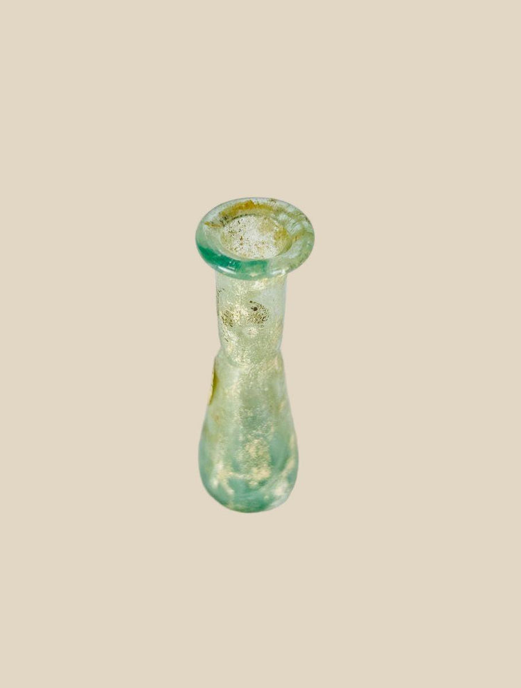 Ancient Roman hand-blown glass bottle, 1st Century BCE–4th Century CE. Elongated cylindrical neck with rounded conical body, out-sprayed folded rim, and delicate translucency. Includes original archaeological tag. Used for ointments, perfumes, or medicines, reflecting Roman glassmaking innovation, daily life, and luxury trade.