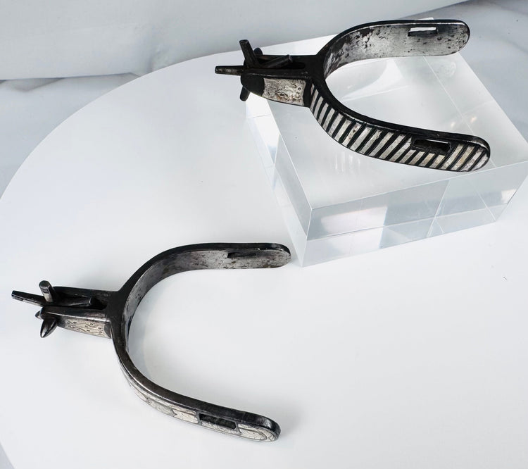 Decorated steel cowboy spurs with silver overlays, strap slots, and aged surface
