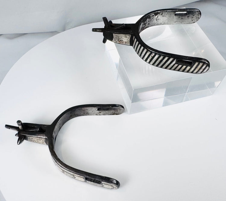 Decorated steel cowboy spurs with silver overlays, strap slots, and aged surface
