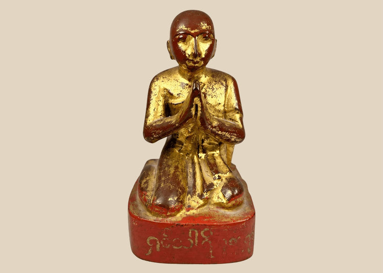 19th-century Burmese wooden monk statue with gold leaf and lacquer remnants, kneeling in Anjali Mudra with serene expression and inscribed base.