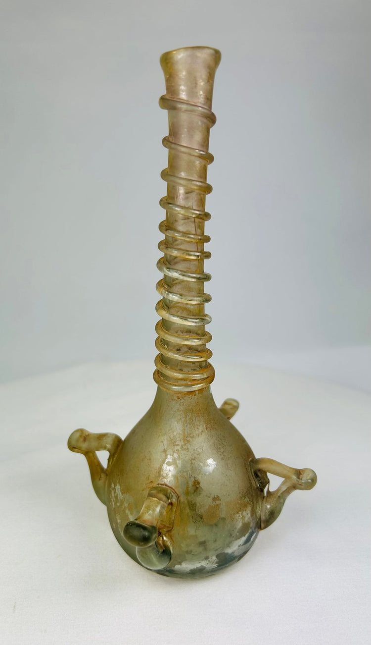 Full-length view of early Islamic glass bottle with elongated neck and iridescent surface, 7.25 inches tall.